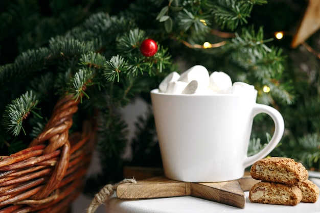 Café em uma xícara branca com marshmallows. Café festivo de manhã com biscoitos de amêndoa cantuccini italianos tradicionais. Uma xícara de café em um fundo de ramos de abeto verde em um suporte branco.