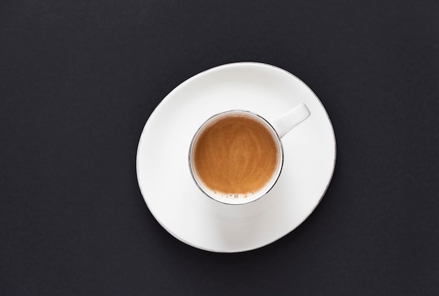 Café em uma xícara branca em um pires branco sobre um fundo preto. O conceito de minimalismo. Postura plana. Copie o espaço.