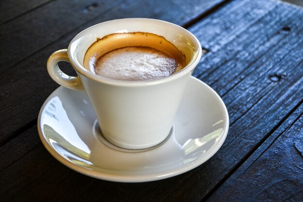 Café em xícara branca na mesa de madeira escura na cafeteria. Cafeteria