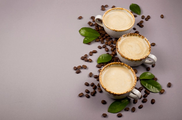 Café em xícaras rústicas entre grãos e folhas de café verde.