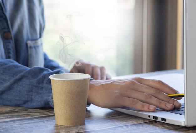 Cafe encima de la mesa de la oficina con una persona que trabaja en la computadora