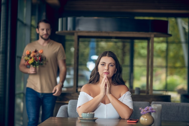 Café, encontro. Mulher bonita séria sentada à mesa esperando e homem sorridente andando atrás