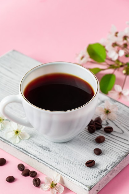 Café espresso fuerte en una bandeja de madera blanca Flores de primavera de un manzano sobre un fondo rosa