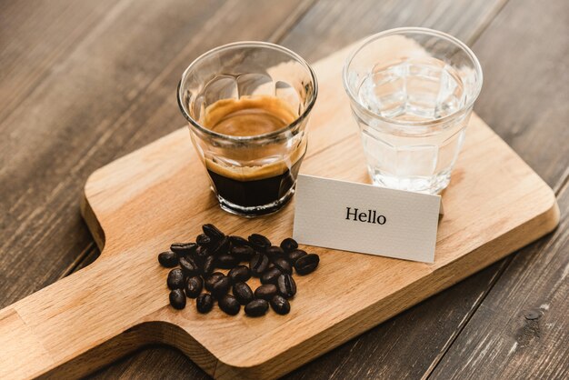 Café espresso negro recién preparado y agua en vasos de chupito servido en bandeja de madera lista para beber