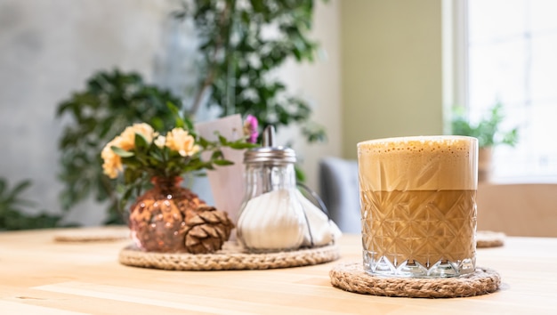 Café con espuma de leche en vaso y jarrón con flores Interior moderno de cafetería o cafetería