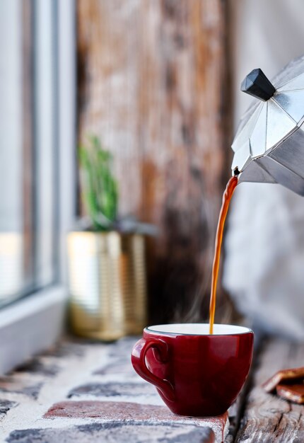 El café expreso se vierte de una cafetera géiser en una taza roja. El vapor sube por encima de la taza. Primer plano, enfoque selectivo