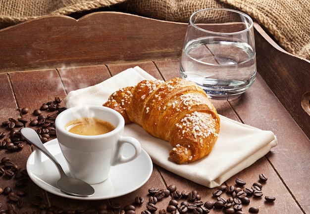 Café expresso com croissant e copo de água.