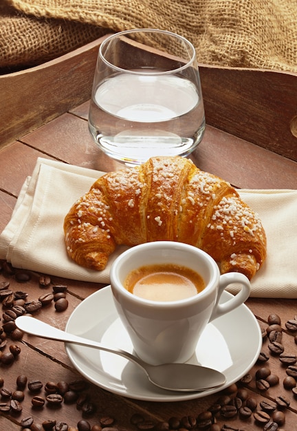Café expresso com croissant e copo de água.