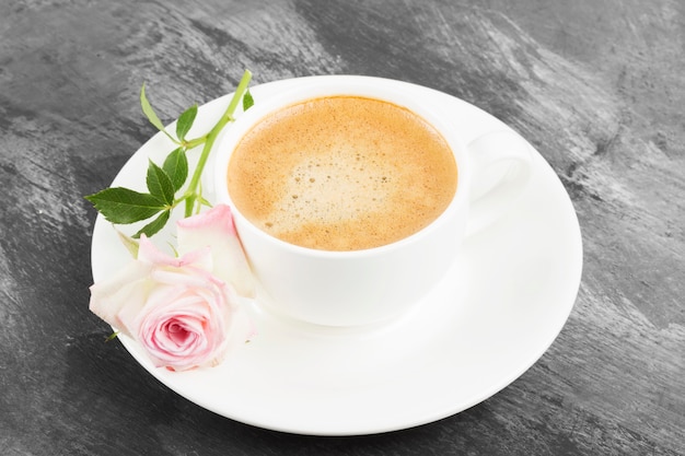 Café expresso em uma xícara branca e uma rosa cor de rosa em um fundo escuro.