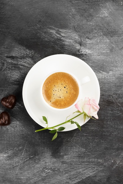 Café expresso em uma xícara branca, uma rosa cor de rosa e chocolates em um fundo escuro. Vista do topo. Fundo de alimentos.