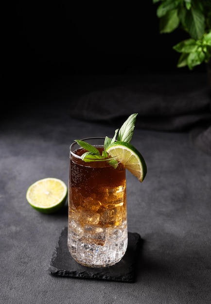 Café fabricado em um copo com gelo tónico e limão em um fundo escuro com frutas cítricas e ervas conceito de artesanato bebida refrescante de tendência