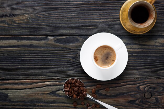 Café fresco e aromático em uma xícara branca e em grãos de café.