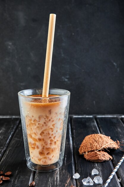 Café gelado em estilo tailandês com leite de coco e grãos de café em uma madeira preta