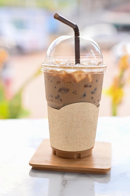 Café gelado em tirar copo copo de plástico na mesa de madeira no café com traçado de recorte no papel de etiqueta em branco para o logotipo do café de maquete