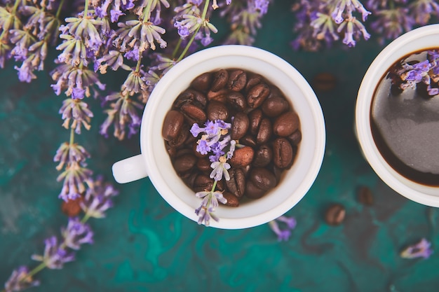 Café, grano de café en tazas y flor de lavanda en la mesa verde desde arriba. Buenos días concepto. Escritorio de trabajo de mujer. Desayuno acogedor Bosquejo. Estilo plano laico