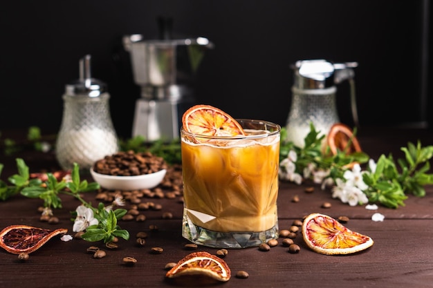 Café helado con leche y rodajas de naranja en una mesa de madera oscura con granos de café Bebida de verano