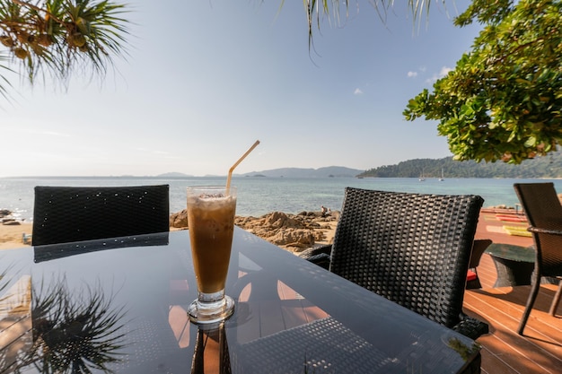Café helado en una mesa de cristal con vistas al mar y a la playa