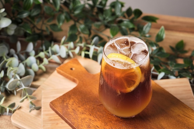 Café helado negro frío mezclado con jugo de limón y rodajas de limón en un vaso con trozos de hielo sobre una mesa de madera luz natural bebida fresca de verano por la mañana