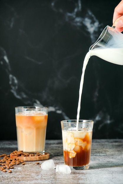 Café helado en un vaso alto con crema vertida, cubitos de hielo y granos en una vieja mesa rústica de madera