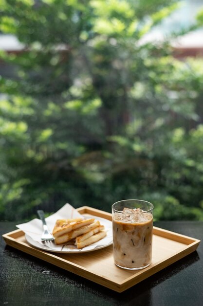 Café helado en vaso sobre mesa de madera y fondo de jardín verde