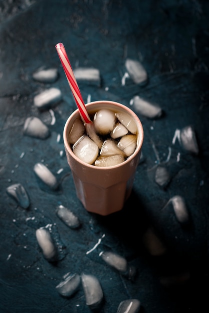 Café helado en un vaso sobre una superficie de piedra azul oscuro con cubitos de hielo. Bebida refrescante del concepto, sed, verano, cola con hielo, vida nocturna, club. Vista plana, vista superior