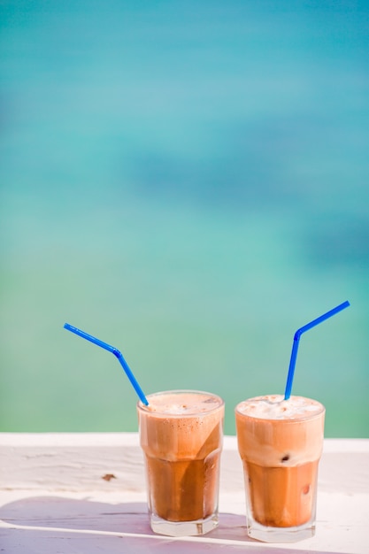 Café helado de verano frappuccino, frappe o latte en un vaso alto en el mar en el bar de la playa