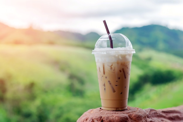 Café de hielo del primer en taza plástica con el fondo hermoso de la montaña.