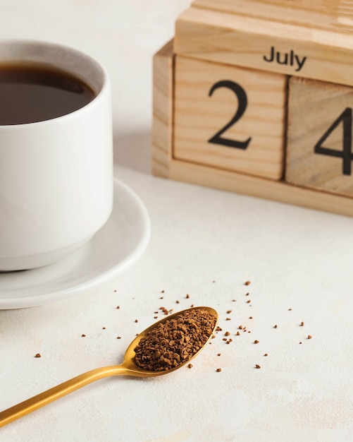 Café instantáneo en una cuchara en el fondo de una taza de café y un calendario de madera en julio cumpleaños ...