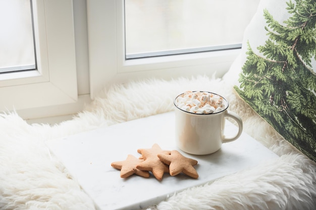 Café de invierno con malvavisco en el acogedor alféizar de la ventana con ramas de abeto navideño