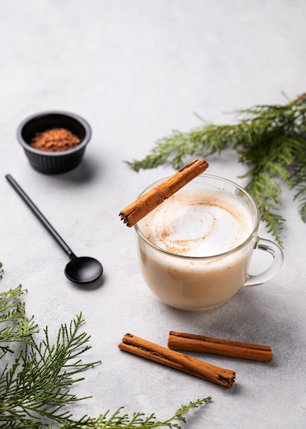 Café latte o capuchino con especias con palitos de canela sobre un fondo claro con ramas de abeto