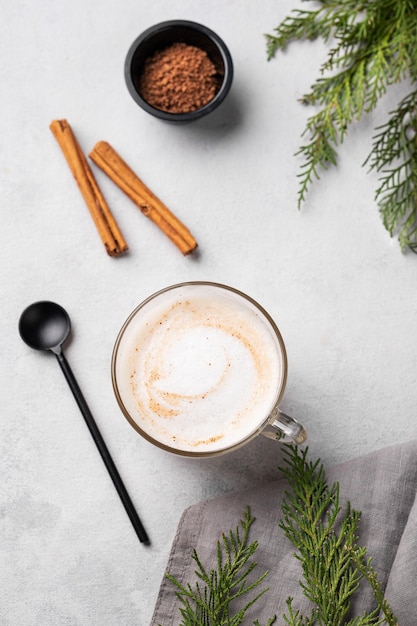 Café latte o capuchino con especias con palitos de canela sobre un fondo claro con ramas de abeto