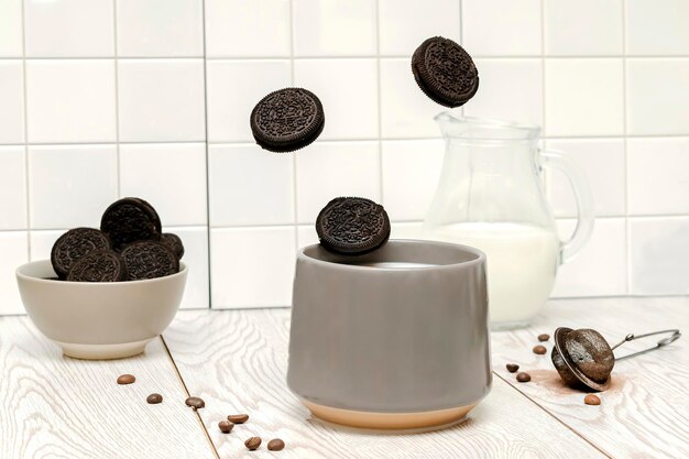 Café con leche cacao con leche y galletas cayendo en taza gris sobre fondo blanco de azulejos de cocina, acción de movimiento de comida flotante de levitación.