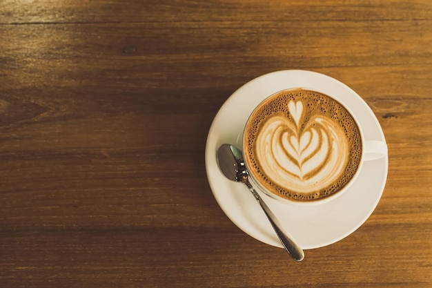 Café con leche caliente con arte de café con leche en forma de espuma de leche en una taza en un escritorio de madera en la vista superior Como desayuno En una cafetería en el concepto de trabajo de negocios durante la cafetería