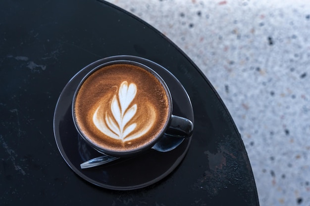 Café con leche caliente con espuma de leche de arte latte en una taza en un escritorio de madera negra en la vista superior Como desayuno En una cafetería en el concepto de trabajo de negocios durante la cafetería
