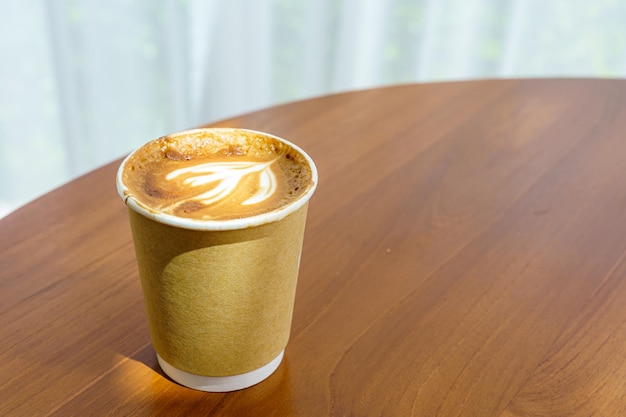 Café con leche caliente con espuma de leche de arte latte en una taza hecha de papel sobre un escritorio de madera en la vista superior Como desayuno En una cafetería en el concepto de trabajo de negocios durante la cafetería