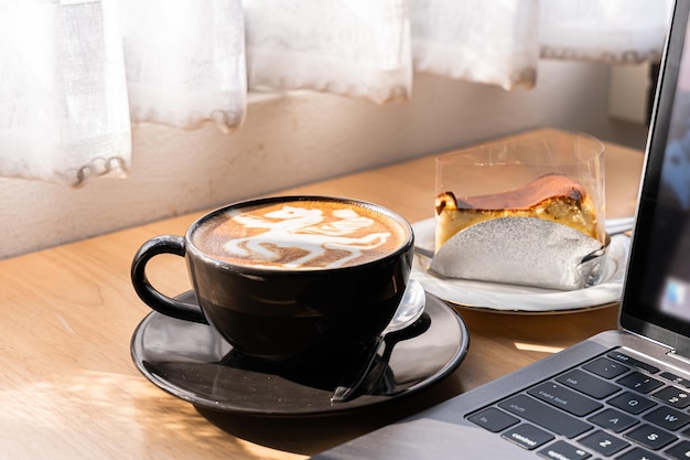 Café con leche caliente con espuma de leche de arte latte en una taza y pastel de chocolate casero y computadora portátil en un escritorio de madera en la vista superior Como desayuno En una cafetería en el café durante el concepto de trabajo empresarial