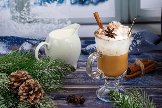 Café con leche caliente con ramas de canela, espolvoreado con canela. Adornos navideños, ramas de un árbol de Navidad. Concepto de vacaciones de año nuevo. Sobre un fondo de madera.