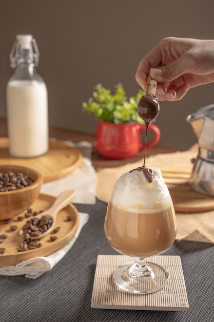 Café con leche helado servido con cobertura de crema batida y jarabe de chocolate en copa de vino en lugar de mesa de madera