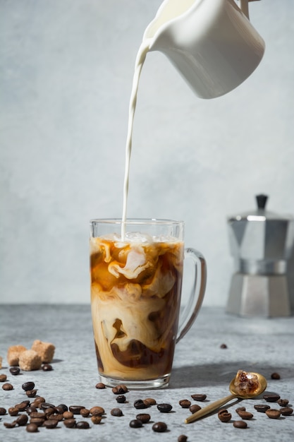 Café con leche helado en vaso con leche vertiendo