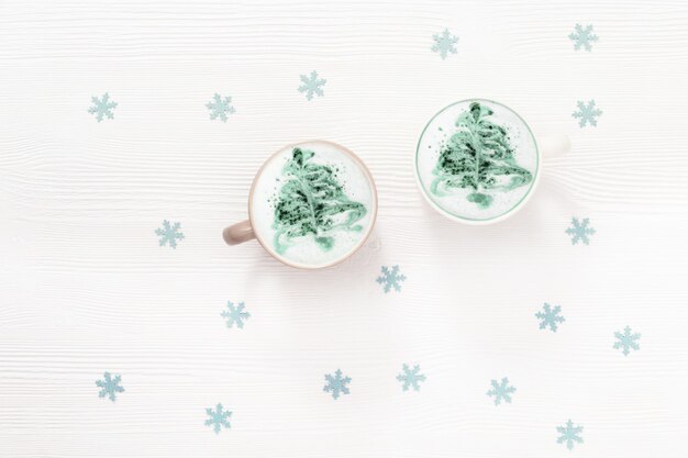 Café con leche de invierno con arte de árbol de año nuevo en taza sobre mesa blanca