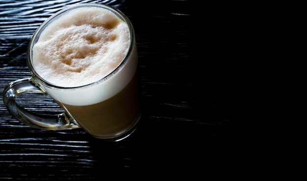 Café con leche en la mesa de madera negra cerca de la ventana