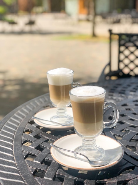 Café con leche o capuchino con espuma de leche en vasos altos en una mesa de hierro forjado en una cafetería callejera de verano