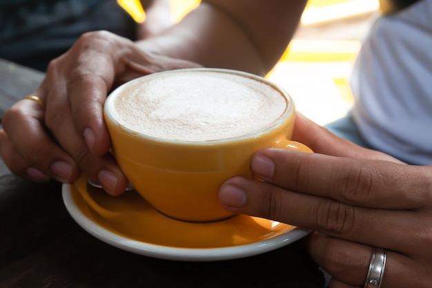 Café con leche en taza amarilla con manos de hombre