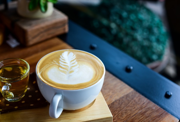 Café con leche en taza blanca en bandeja de madera.