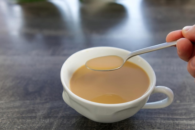 Café con leche en una taza blanca La mano remueve el café con una cuchara Una gota de café cae en una taza