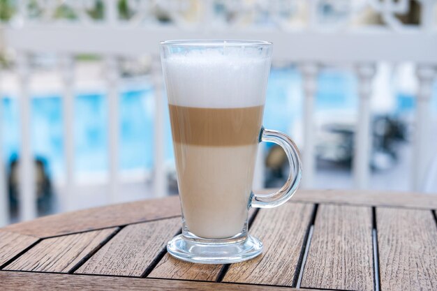 Un café con leche en una taza de vidrio está sobre una mesa en un café. Terraza de verano.