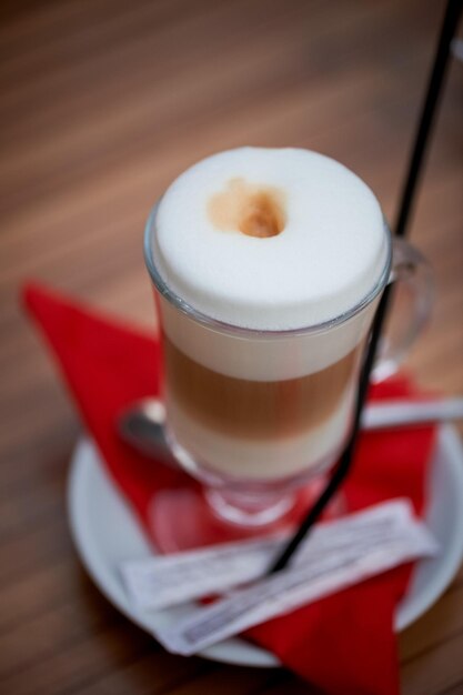 Café con leche en una taza de vidrio con mango de espuma alta De pie sobre una servilleta roja