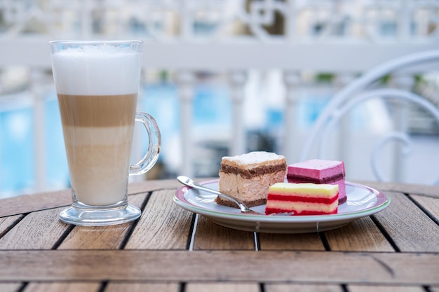 Café con leche en una taza de vidrio y un pastel está sobre la mesa en un café. Terraza de verano.