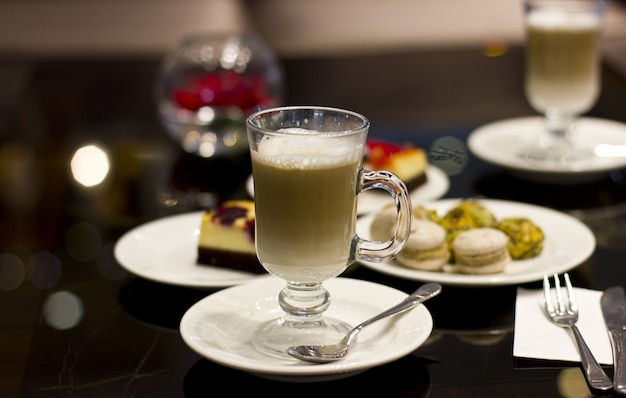 Café con leche en un vaso con la cuchara de plata y pastelería