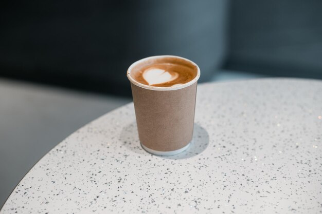 Café con leche en un vaso de papel servido en una mesa blanca en el café